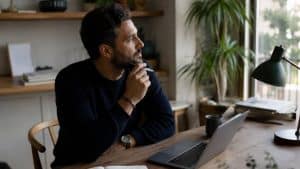 What Is the Difference Between IOP and Partial Hospitalization hero image of a man thinking about the difference while starting out at window.